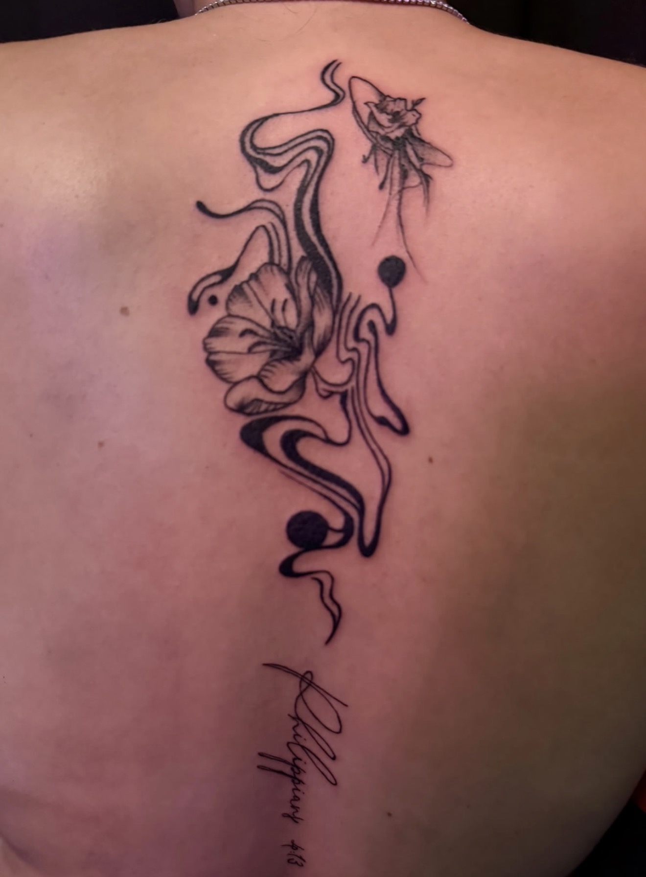 Fine line poppy and flowing abstract linework tattooed along the spine with script below, by Peter Albert at Warpath Studio.